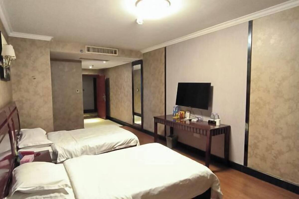 A hotel room with two single beds, a flat-screen TV, a small table with a lamp, and a mirror.