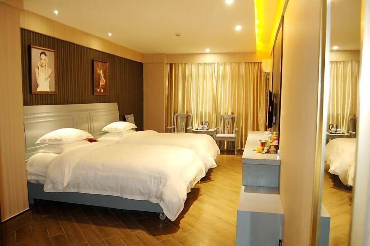 A hotel room with a large bed, a desk, two chairs, a mirror, and a television.
