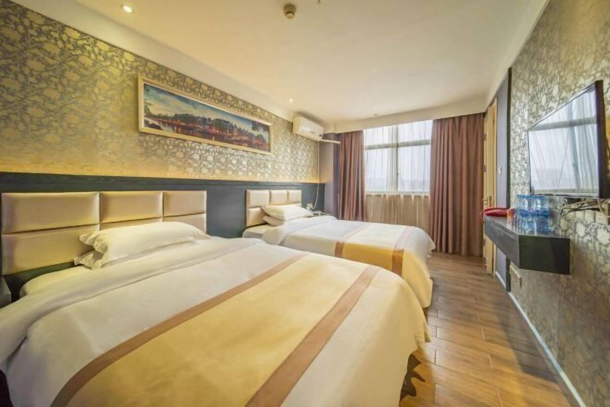 A hotel room with two beds, a painting on the wall, a TV, and a window with curtains.