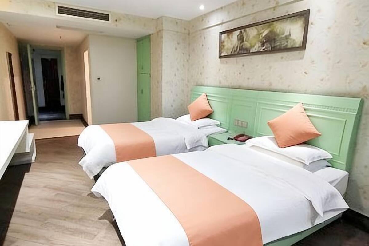 A hotel room with two beds, a green headboard, a painting on the wall, and a wooden floor.