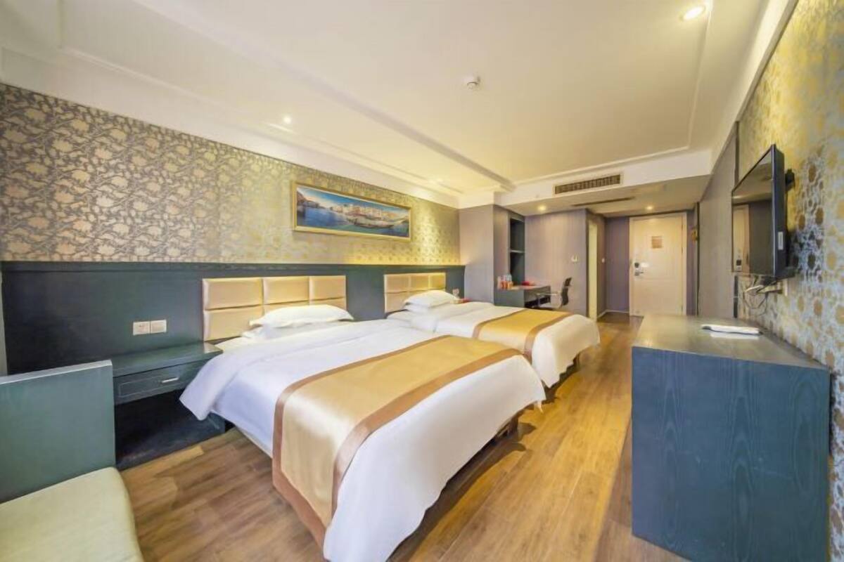 A hotel room with two beds, a desk, a TV, and a bathroom.