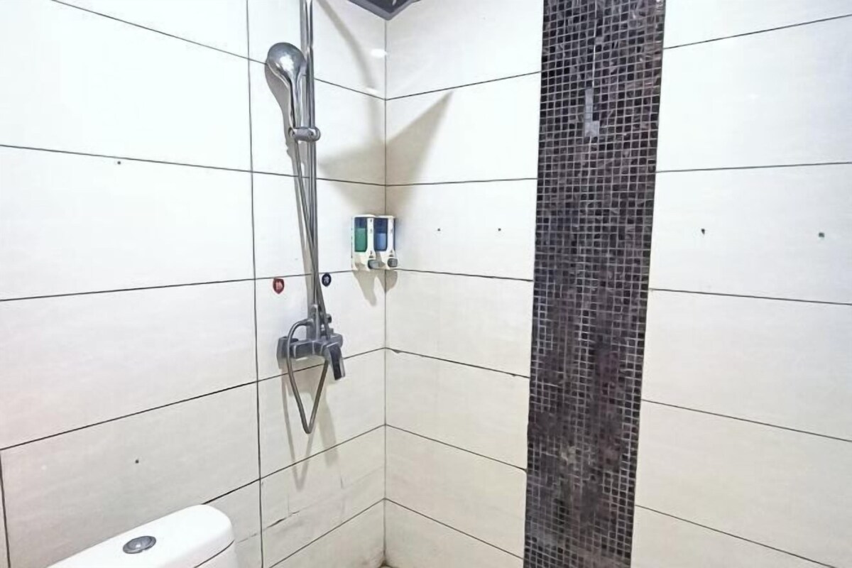 A bathroom with white tiled walls, a shower with a chrome fixture, and a small control panel.