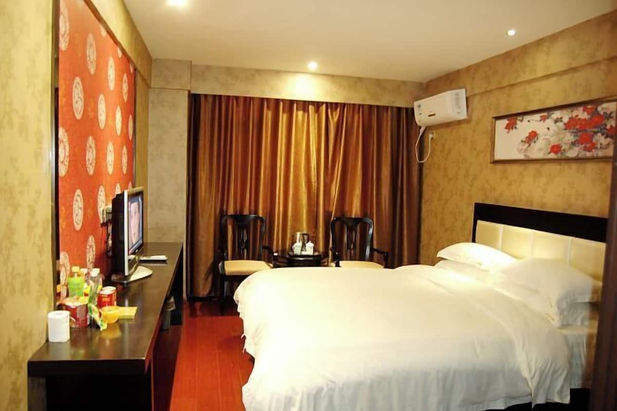 A hotel room with a bed, a desk with a television, a chair, and a small table.