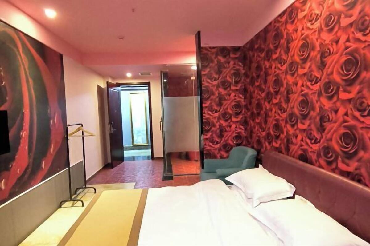 A hotel room with a bed, a mirror, a wardrobe, and a red floral wallpaper.