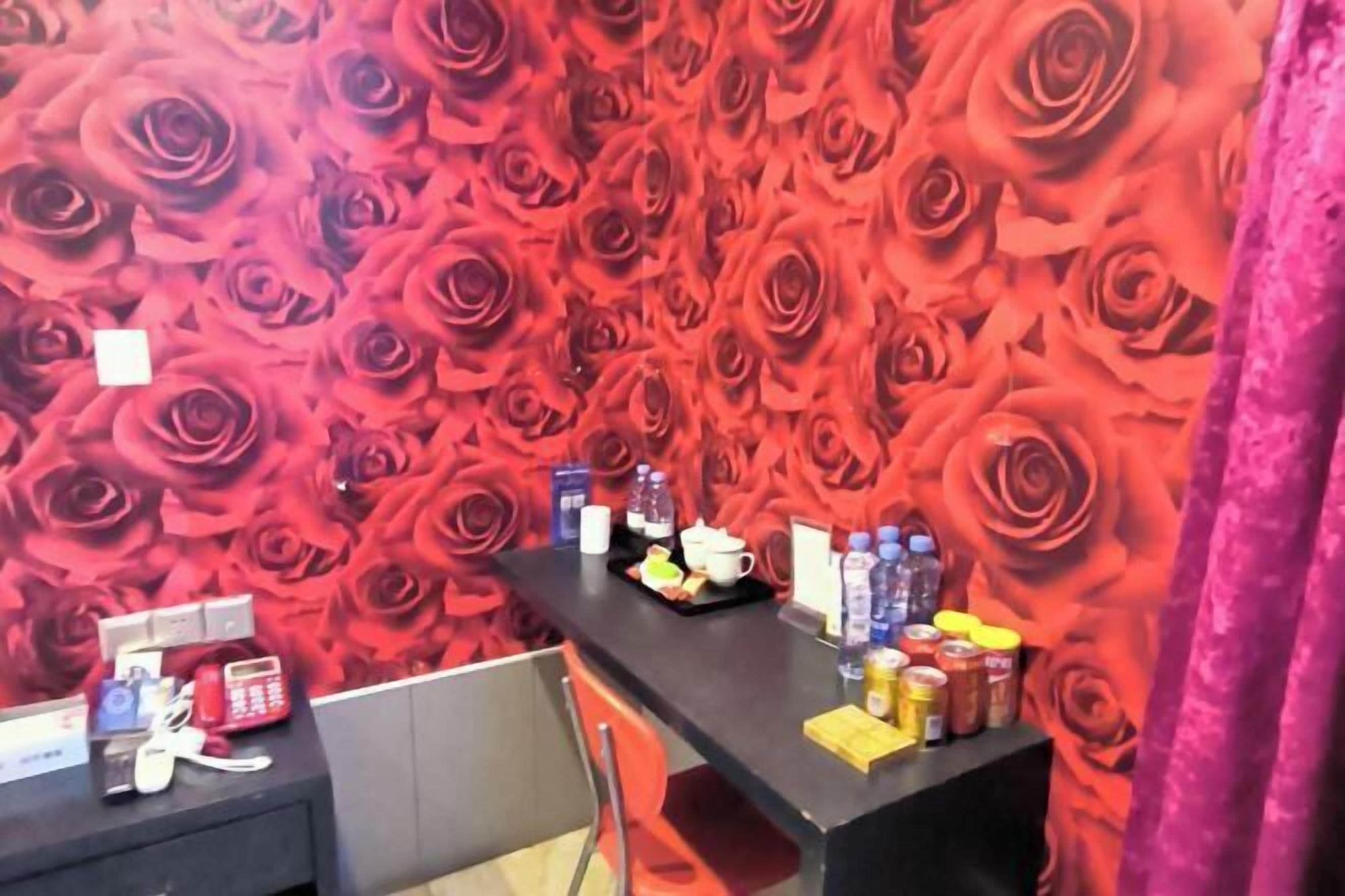 Una habitación con papel tapiz de rosas rojas, un escritorio negro con varios objetos y una silla roja.