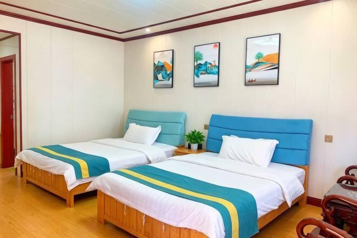 Een hotelkamer met twee bedden, houten vloeren, een klein tafeltje en drie aan de muur hangende schilderijen.