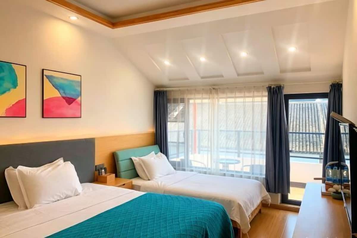 Een hotelkamer met twee bedden, een groot raam met gordijnen en uitzicht op de omgeving.