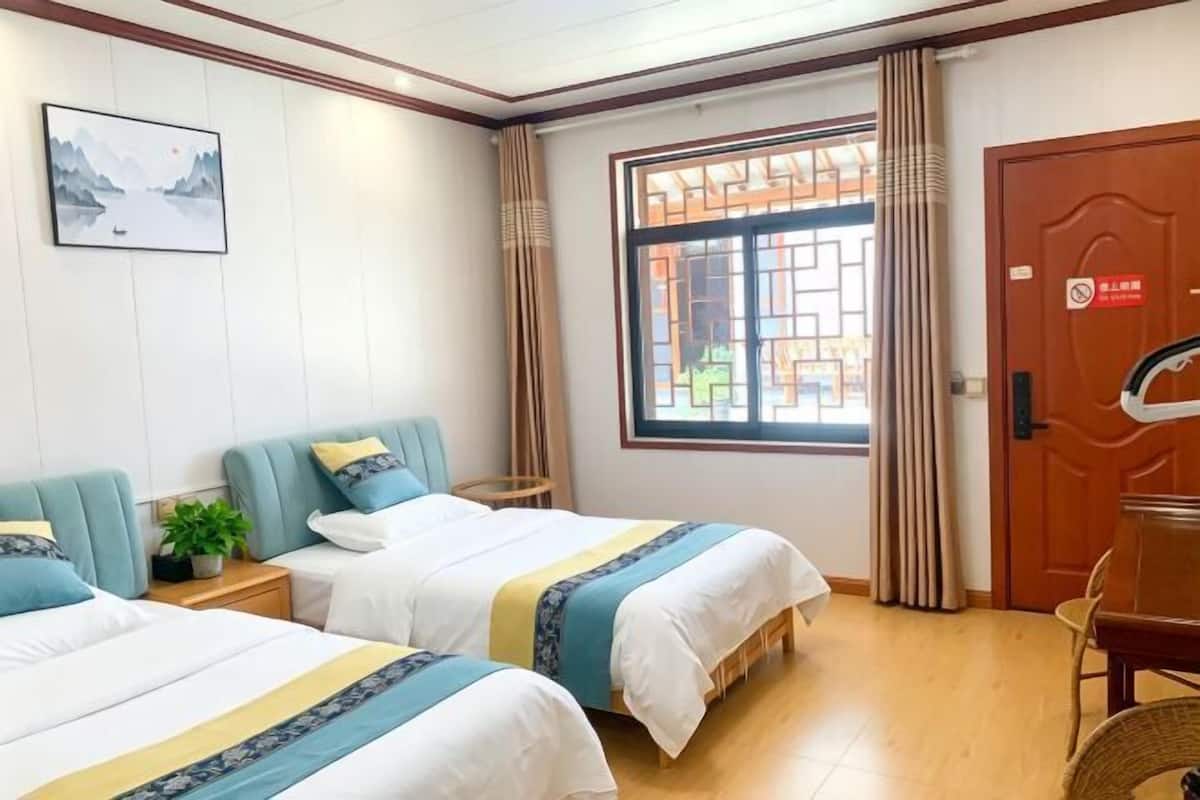 Een hotelkamer met twee bedden, een raam met gordijnen, een deur met een bordje en een ingelijst schilderij aan de muur.