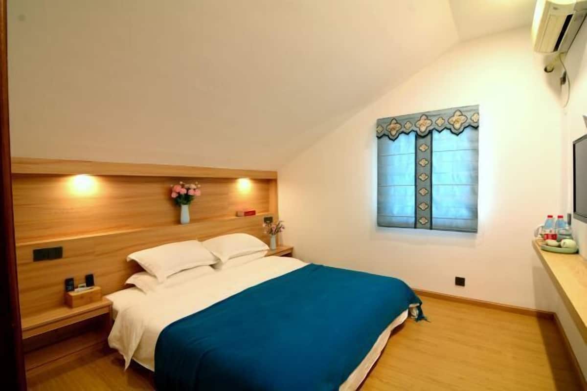 Een slaapkamer met een bed, nachtkastjes, een raam met decoratieve gordijnen en een wandairconditioner.