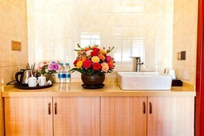 Ein Hotelbad mit einem Waschbecken, einem Blumenstrauß und Pflegeprodukten auf der Ablagefläche.