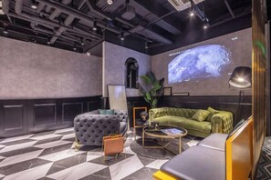 A modern lounge area with a sofa, ottoman, and coffee table, a large screen displaying a projection, and a plant. - Shanghai Jinli S Hotel (Lujiazui Bund Branch) (Shanghai)