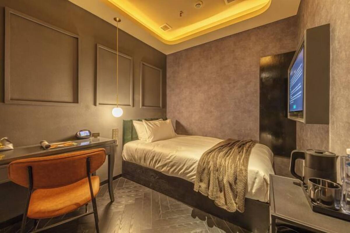 A modern hotel room with a bed, desk, chair, and a TV mounted on the wall.