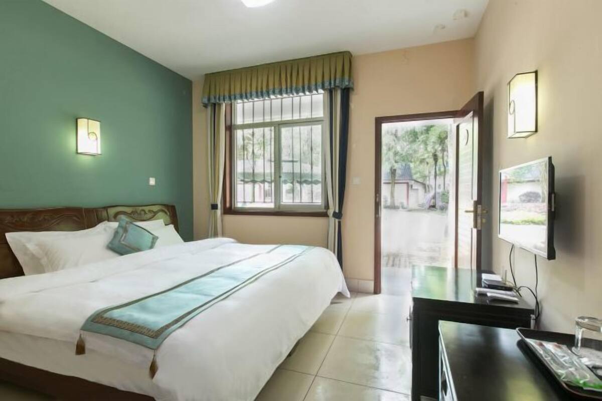 Quarto de hotel com cama, escrivaninha, televisão e janela com cortinas.