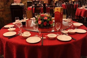 A round dining table with a red tablecloth, white plates, and a centerpiece of flowers. - Cuiyuezhuang Countryside Hotel (Dujiangyan)
