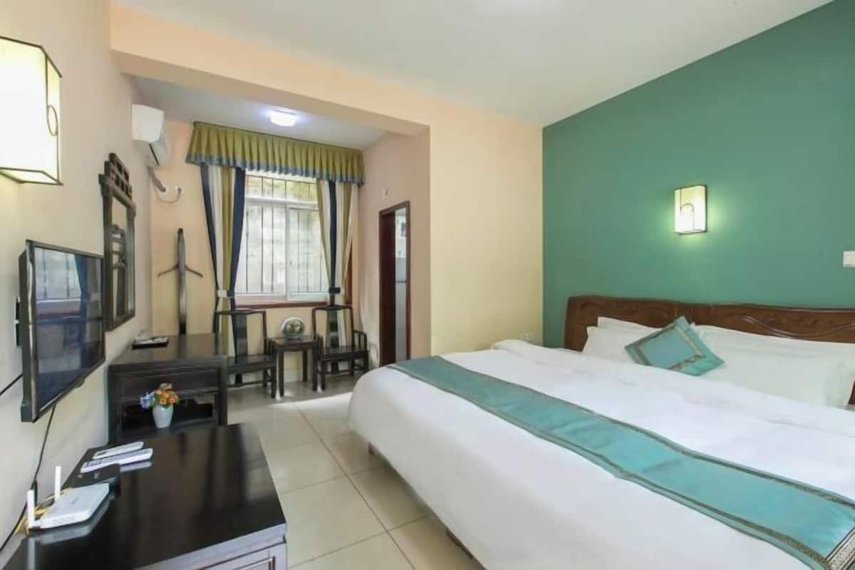 Quarto de hotel com cama, escrivaninha, cadeira, televisão e janela com cortinas.