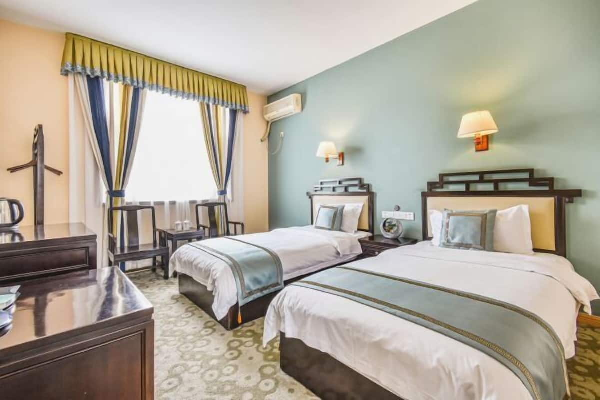 Quarto de hotel com duas camas, uma escrivaninha, uma cadeira, uma luminária e um ar condicionado.