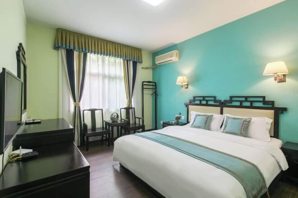 Quarto de hotel com cama, escrivaninha, cadeira, luminária e ar-condicionado fixado na parede.