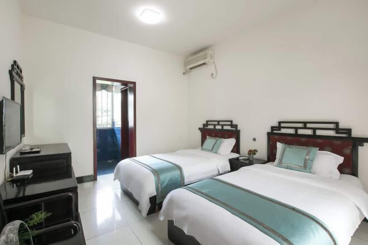 Quarto de hotel com duas camas, uma escrivaninha com computador, televisão e ar condicionado.