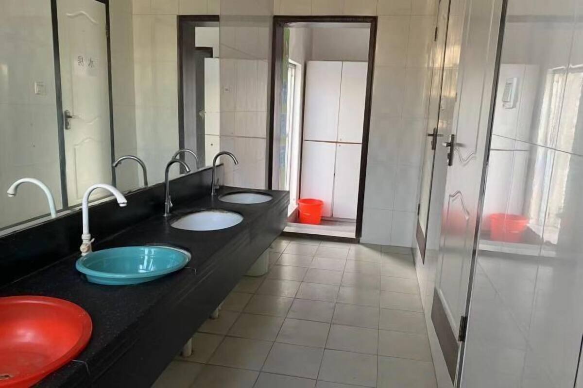 A public restroom with three sinks, a mirror, and a door leading to another room.
