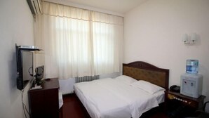 A hotel room with a bed, a desk with a computer, a water dispenser, and a wall-mounted TV. - Industry Hotel (Zhaoyuan)