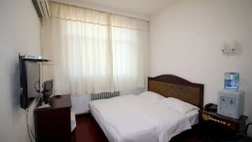 Habitación de hotel con cama, escritorio, silla, dispensador de agua y lámpara de pared.