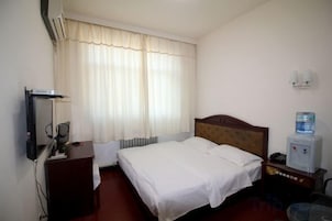 Habitación de hotel con cama, escritorio, silla, dispensador de agua y lámpara de pared.