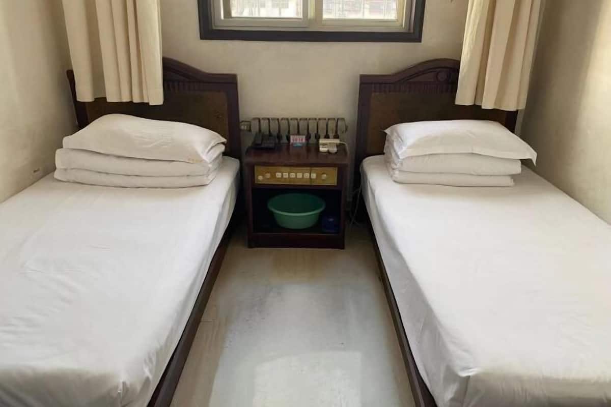 A small room with two single beds, a nightstand with a green bowl, and a window above the beds.