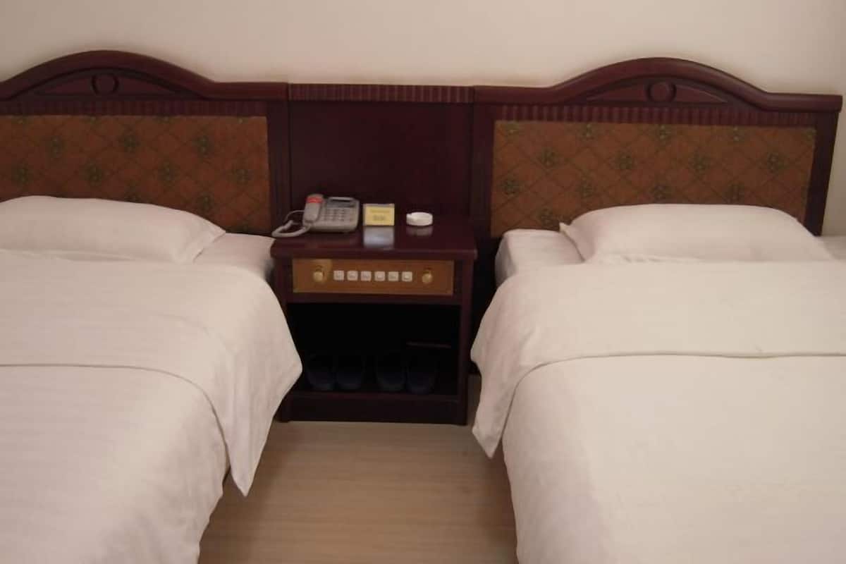 A hotel room with two beds, a wooden headboard, a nightstand with a phone, and a shoe rack.