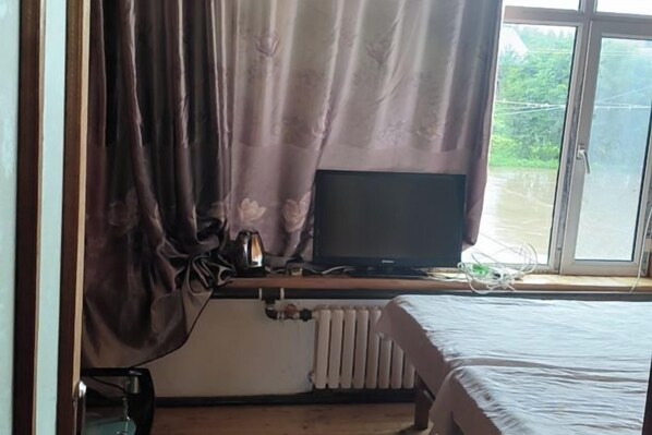 Una habitación con cama, ventana con cortinas, radiador y televisor sobre un mueble.