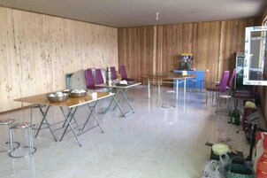 Ein Zimmer mit einem langen Esstisch, mehreren Stühlen, einer kleinen Küchenzeile und einem Fernseher.