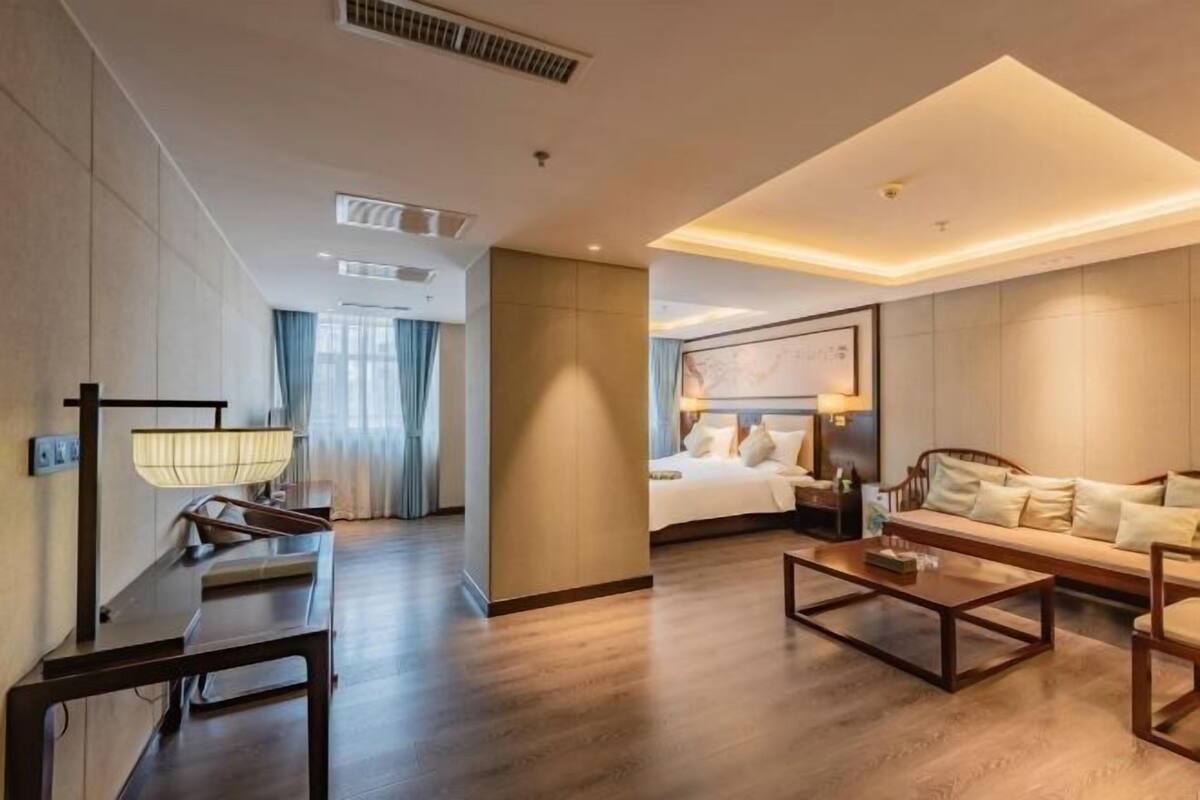 Ein Hotelzimmer mit Holzboden, einem Bett mit weißer Bettwäsche, einer Couch, einem Couchtisch und einem Schreibtisch mit Lampe.