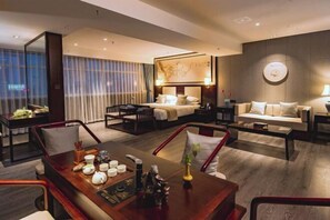 A hotel room with a bed, a sofa, a dining table with tea set, and a large window with curtains. - Huawen International Hotel (Shijiazhuang)