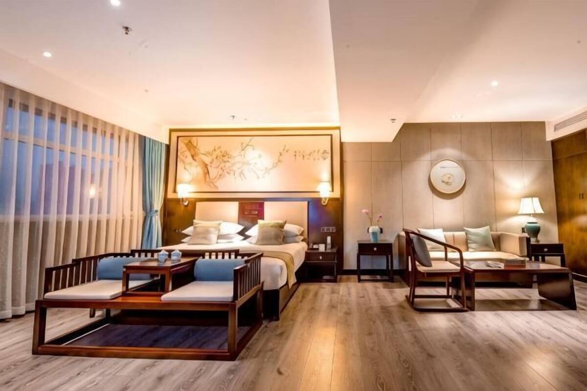 Ein Hotelzimmer mit Bett, Nachttischen, einer Couch, einem Sessel, einem Couchtisch und einem großen Kunstwerk über dem Bett.