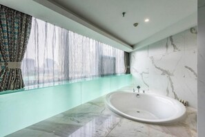 A modern bathroom with a large bathtub, a glass shower enclosure, and a view of the city through sheer curtains. - Huawen International Hotel (Shijiazhuang)