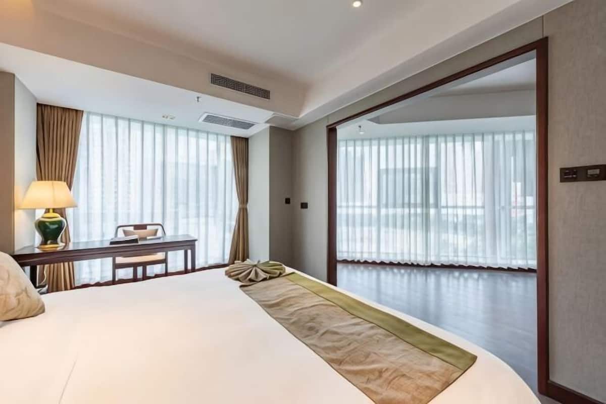 Ein Hotelzimmer mit einem großen Bett, einem Schreibtisch mit Lampe, einem Sessel und Blick durch eine Glastür.
