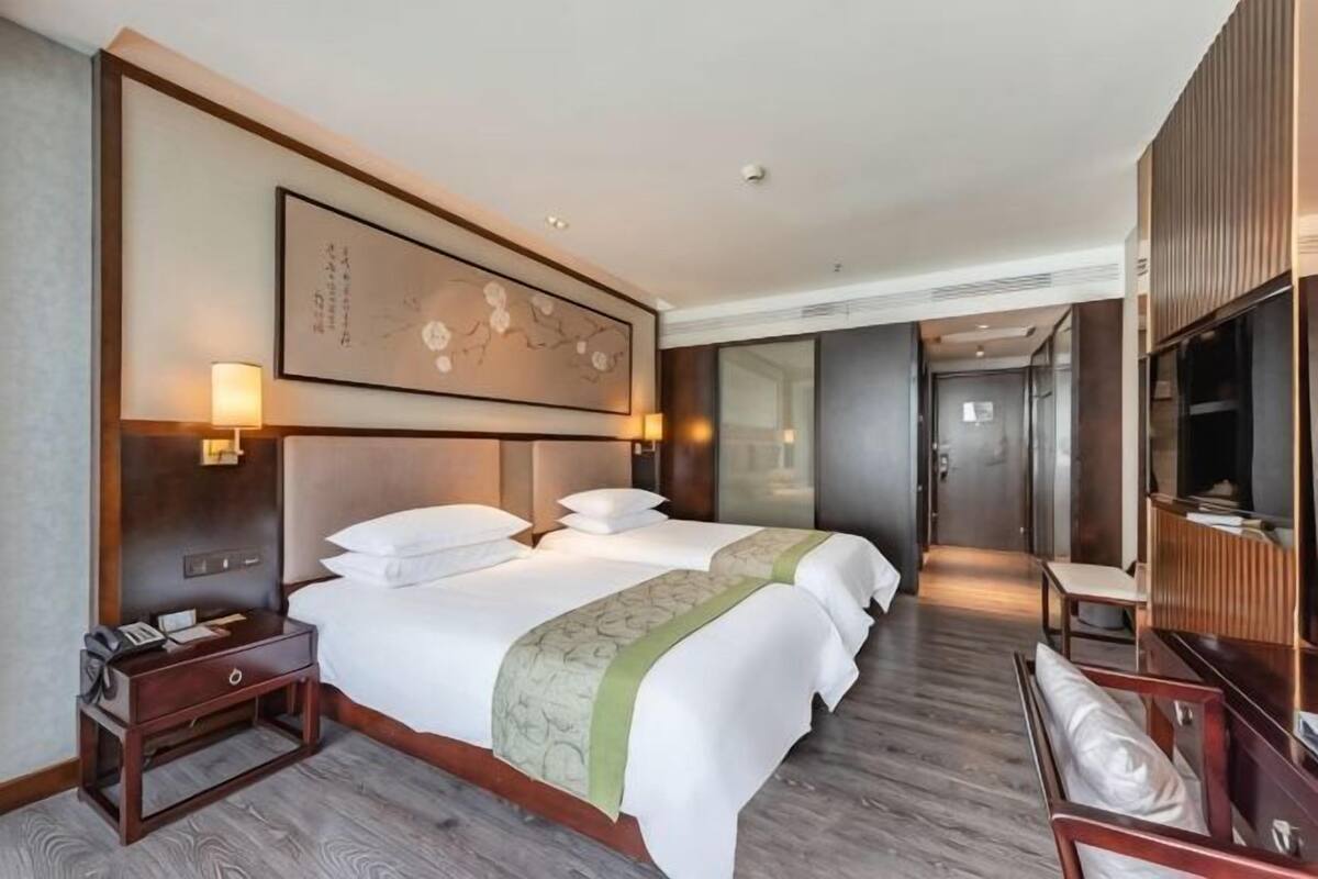 Ein Hotelzimmer mit zwei Betten, einem Nachttisch, einem Fernseher und einem großen Kunstwerk an der Wand.