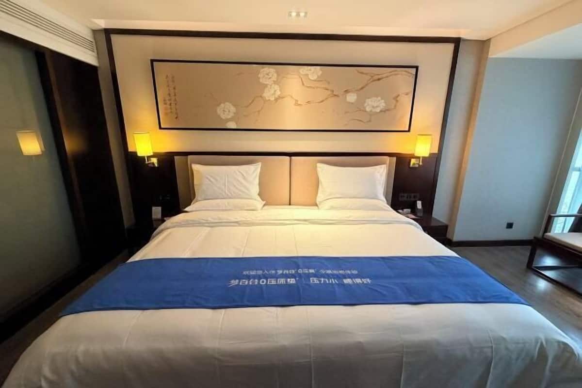Ein Hotelzimmer mit einem großen Bett, zwei Nachttischen, einem Wandbild und einer blauen Bettdecke.