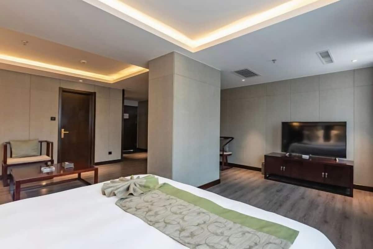 Ein modernes Hotelzimmer mit einem großen Bett, einem Flachbildfernseher, einem Holztisch und einer Couch.
