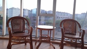 Three wicker chairs and a small round table in a room with large windows. - Lianyungang Green Apple Hotel Apartment (Lianyungang)