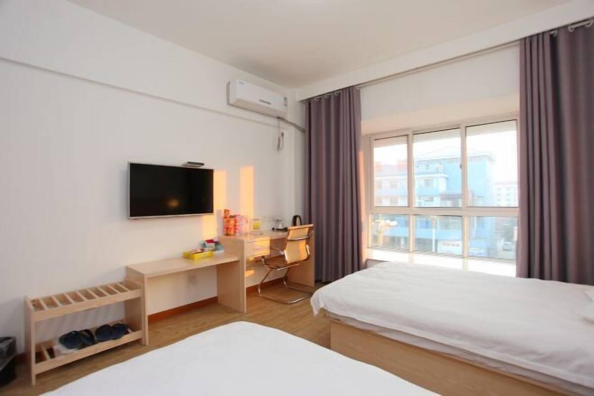 A hotel room with two beds, a desk with a chair, a TV, and a window with curtains.