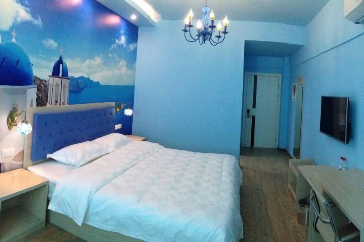 A bedroom with a bed, a desk, a TV, and a mural of a blue sky and sea.