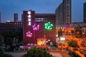 Un hotel con un llamativo letrero de neón, un área de estacionamiento y un paisaje urbano al fondo.