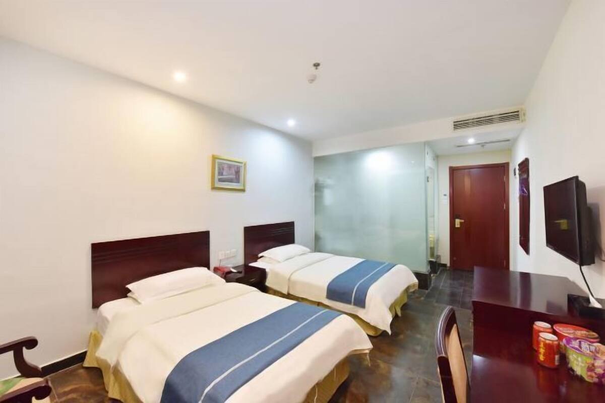 A hotel room with two beds, a desk, a chair, a television, and a door leading to another room.
