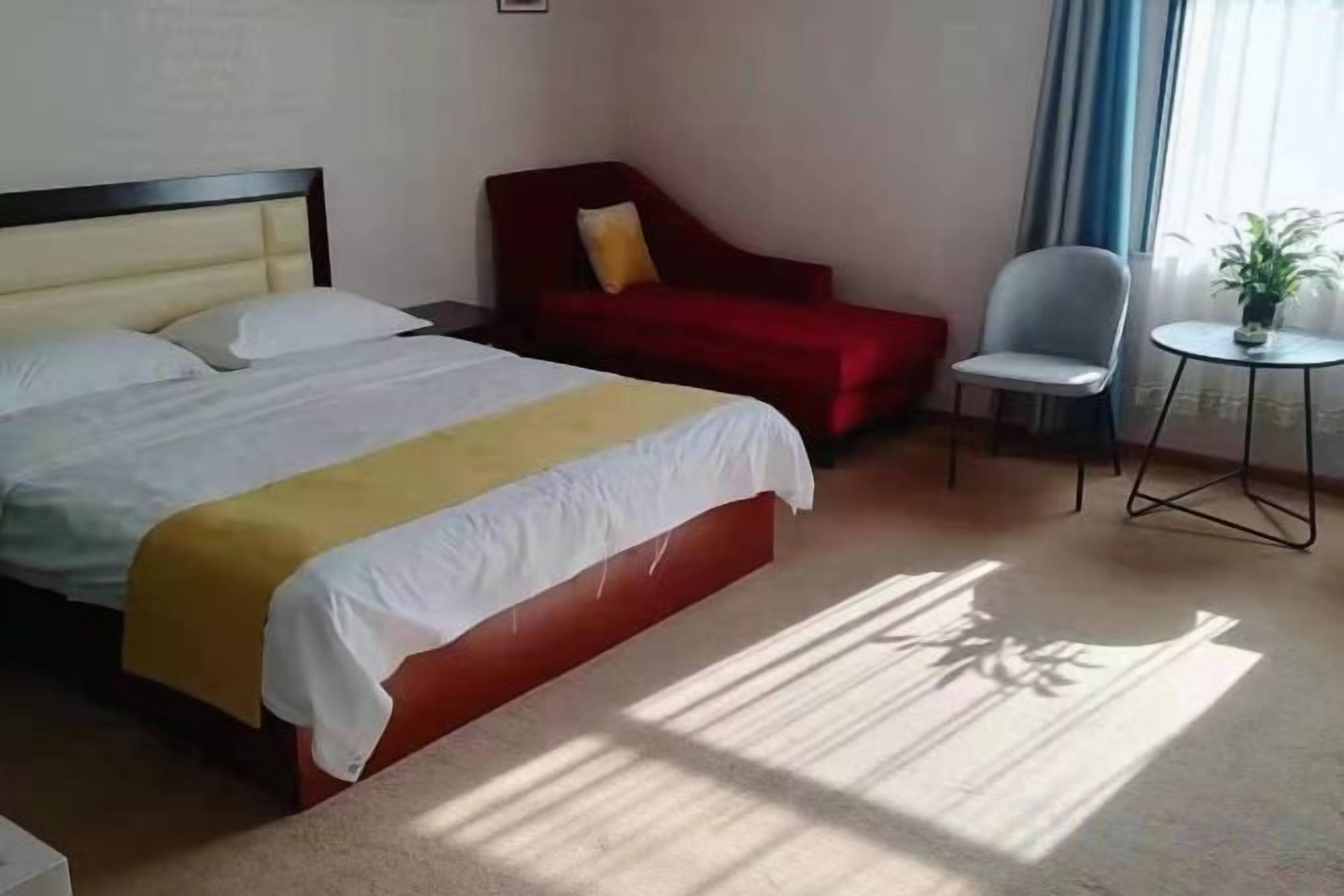 A hotel room with a bed, a red sofa, a small table, and a chair.