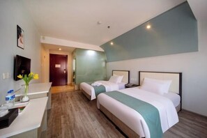 Ett hotellrum med två sängar, ett skrivbord, en tv och ett badrum som syns genom en öppen dörr.