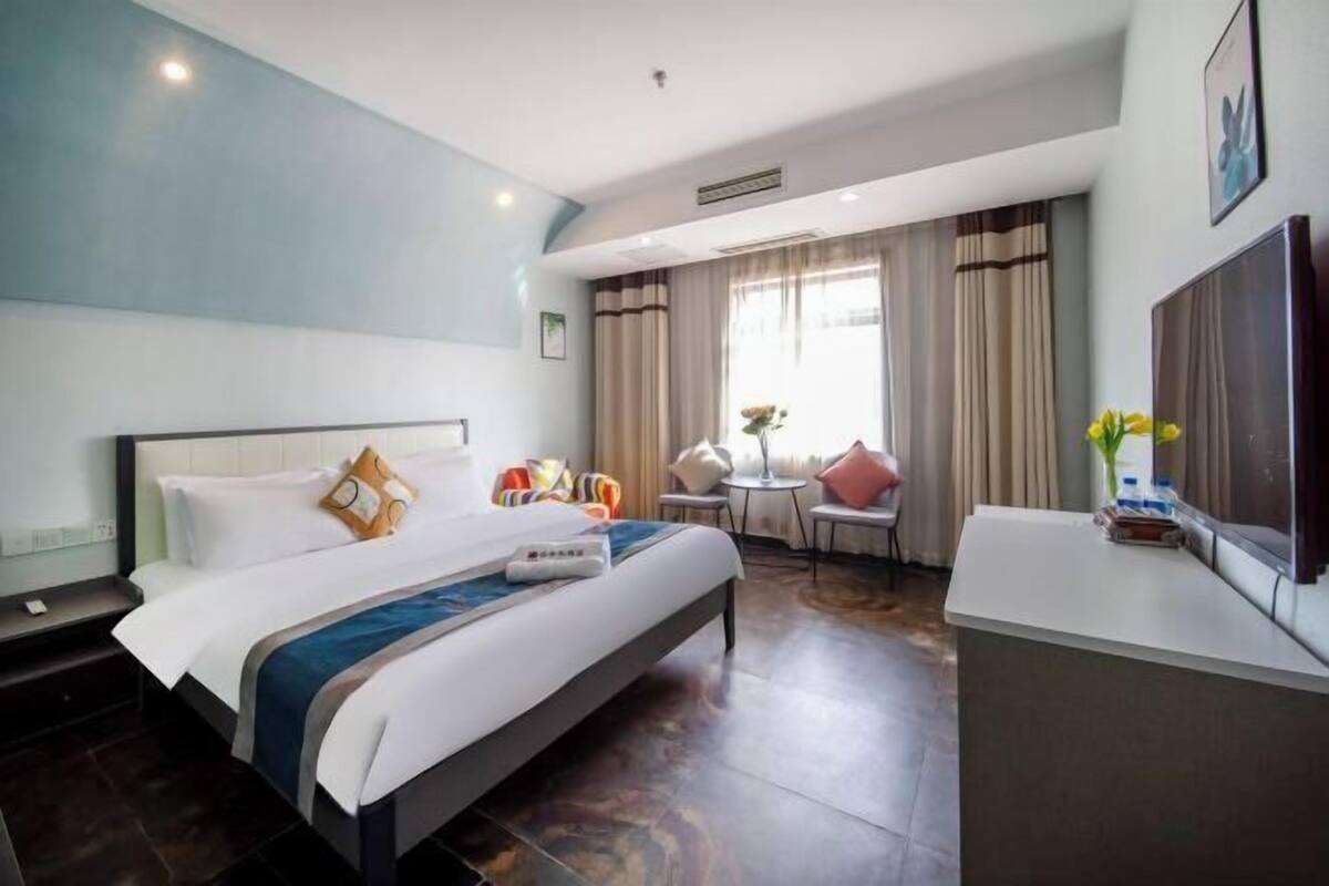 A hotel room with a bed, a desk, a chair, a TV, and a window with curtains.