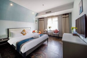A hotel room with a bed, a desk, a chair, a TV, and a window with curtains.