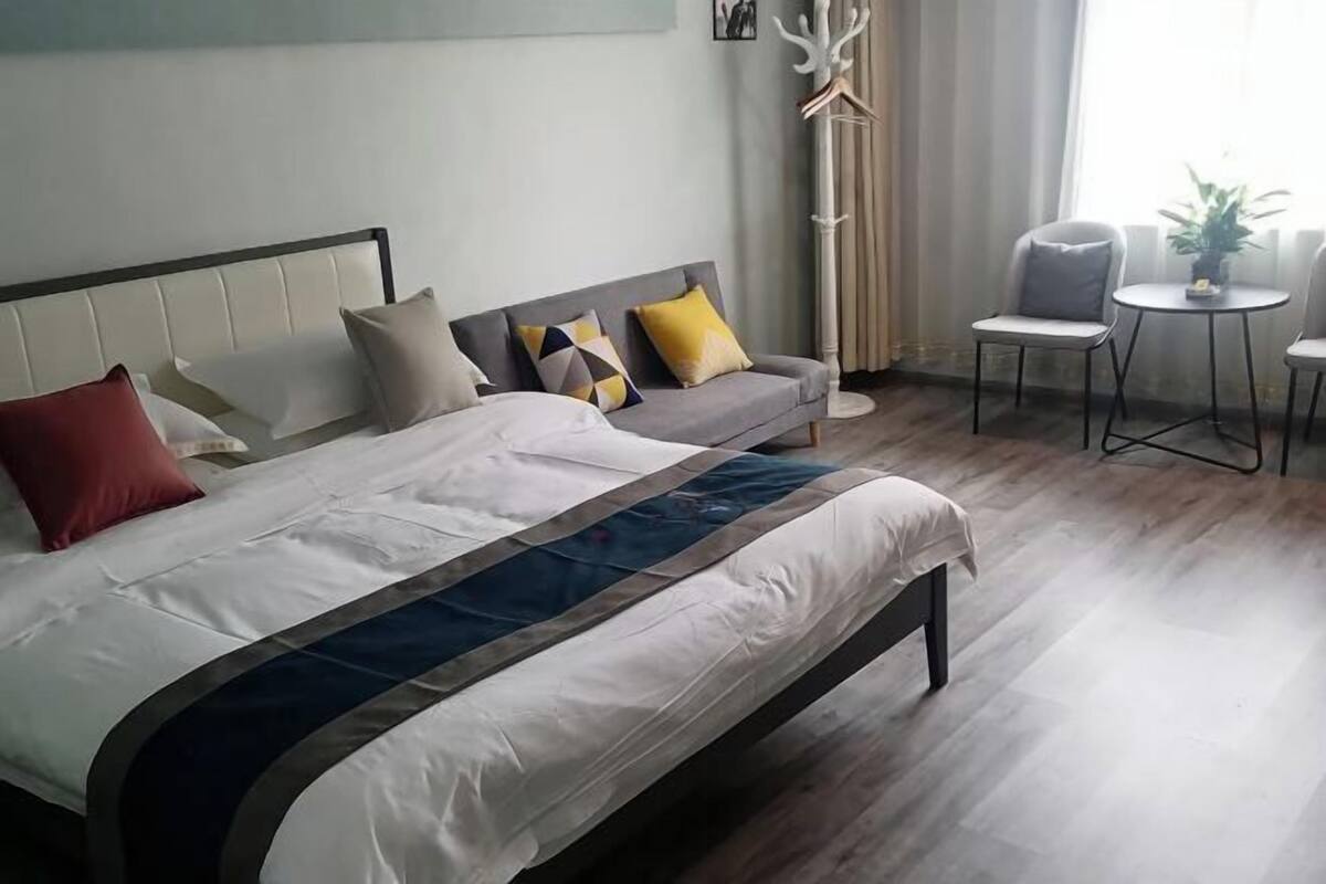 A hotel room with a bed, a sofa, a chair, a small table, and a coat rack.