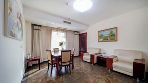 A hotel room with a dining area, two sofas, a painting, and a large window with curtains. - Yu'an Hotel (Lu'an Guangcai Great Market Railway Station) (Lu'an)