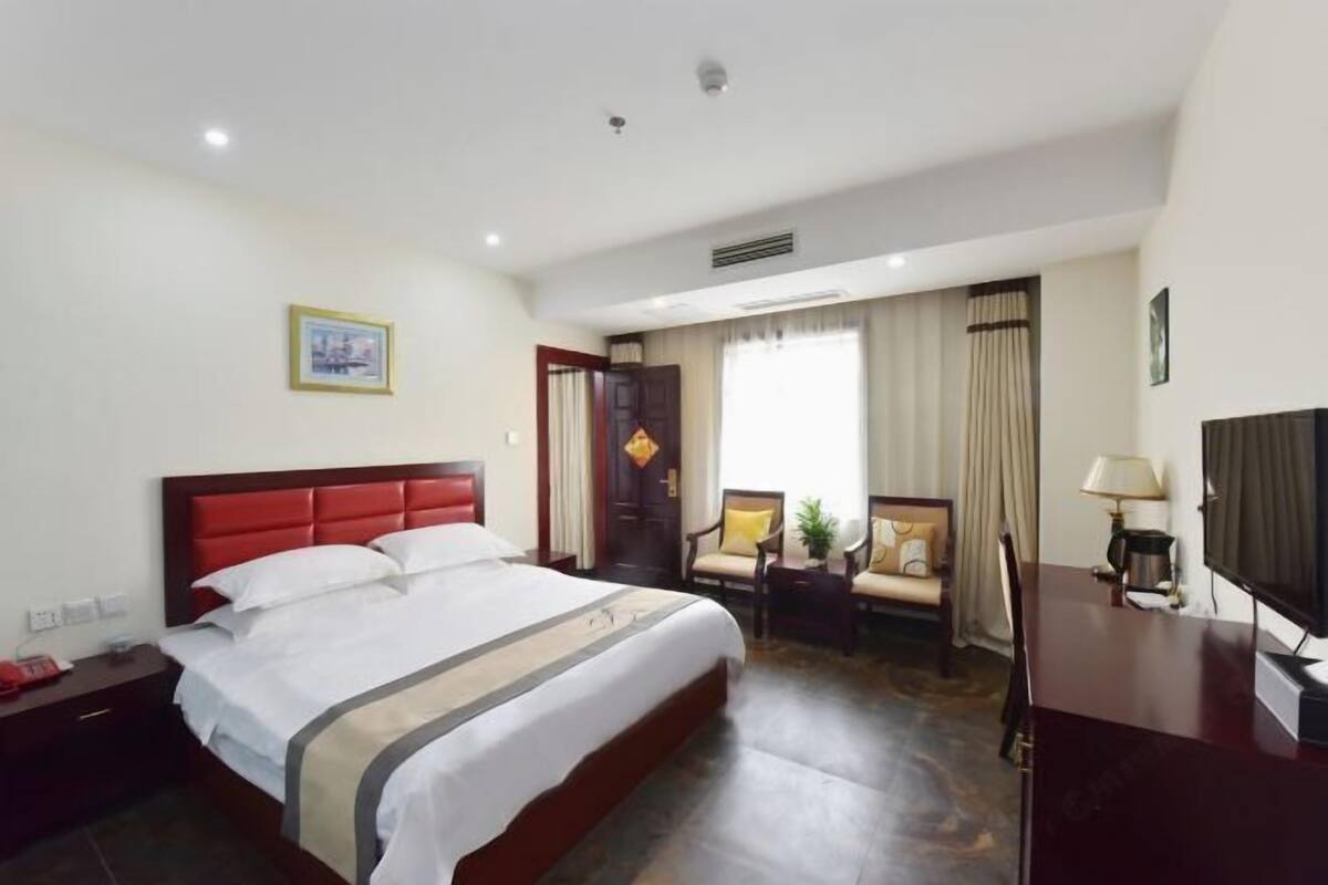 A hotel room with a large bed, a desk, a chair, a TV, and a window with curtains.